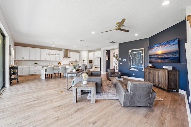 living room with visible vents, light wood-style floors, baseboards, recessed lighting, and ceiling fan with notable chandelier