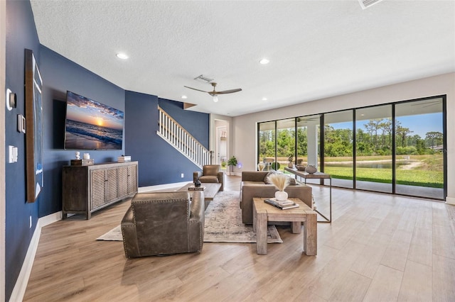 living area with stairs, a ceiling fan, baseboards, and wood finished floors