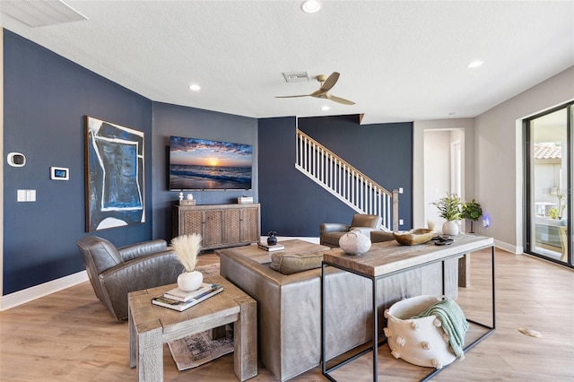 living room featuring stairway, ceiling fan, light wood finished floors, and visible vents