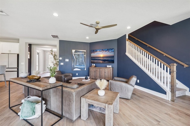 living room featuring stairs, ceiling fan, and light wood finished floors