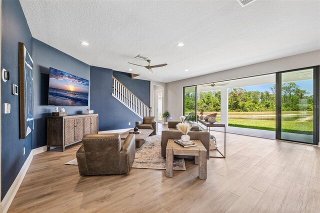 living area featuring wood finished floors, baseboards, ceiling fan, stairway, and a textured ceiling