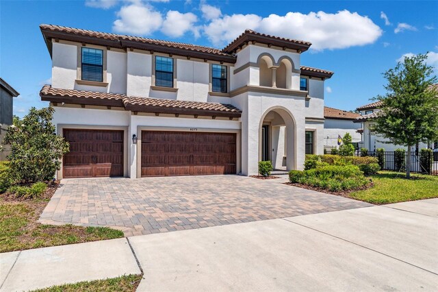 mediterranean / spanish house with decorative driveway, an attached garage, fence, and stucco siding
