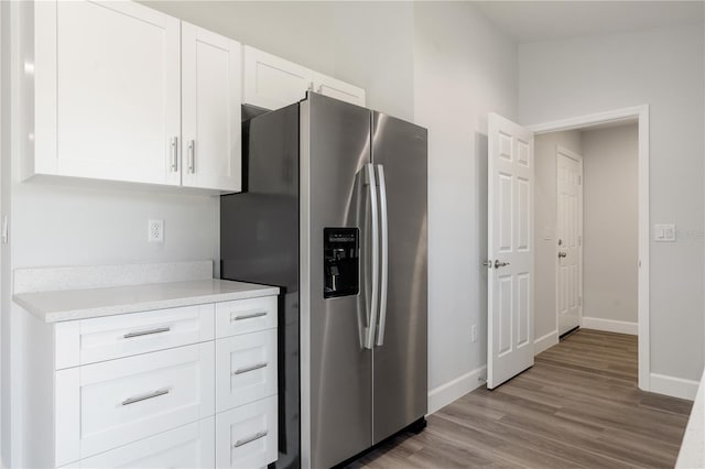 kitchen with white cabinets, baseboards, stainless steel fridge, and light wood-style flooring
