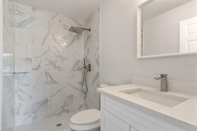 full bathroom with toilet, tiled shower, and vanity