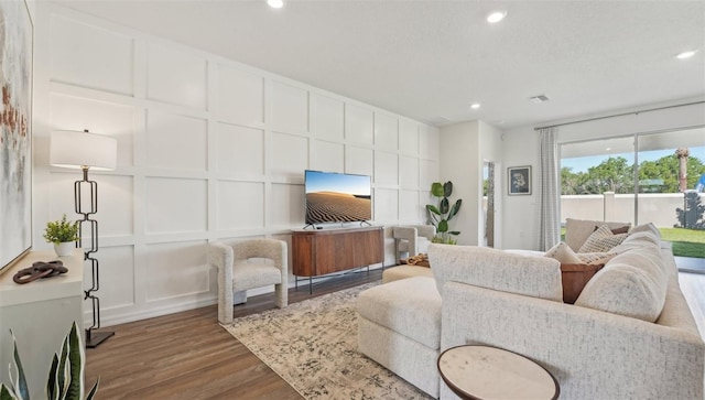 living area featuring a decorative wall, recessed lighting, wood finished floors, and visible vents