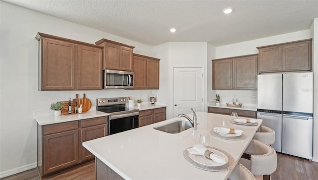 kitchen featuring a sink, appliances with stainless steel finishes, dark wood-style flooring, and an island with sink