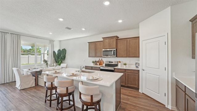 kitchen featuring a textured ceiling, appliances with stainless steel finishes, brown cabinetry, and a sink