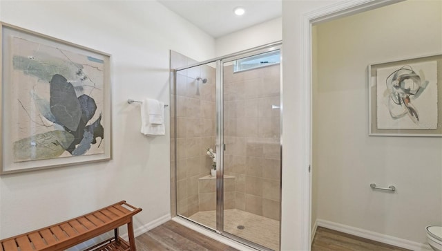 bathroom featuring toilet, baseboards, wood finished floors, and a stall shower
