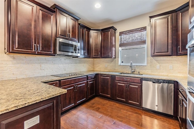 kitchen featuring light stone counters, a sink, stainless steel appliances, tasteful backsplash, and dark wood-style floors