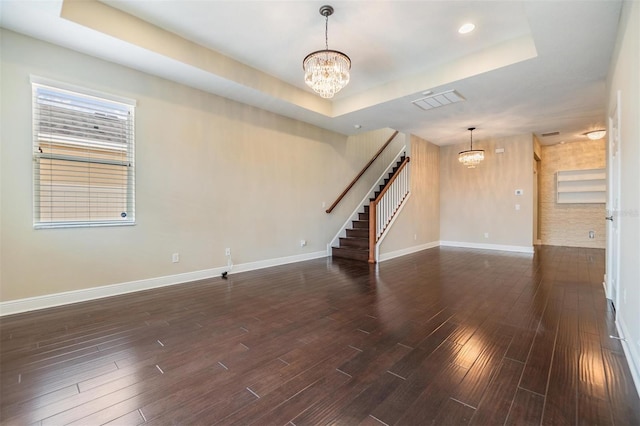 unfurnished living room with an inviting chandelier, baseboards, a raised ceiling, and stairs