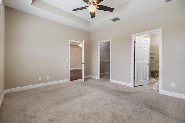 unfurnished bedroom featuring visible vents, a raised ceiling, baseboards, a spacious closet, and carpet flooring