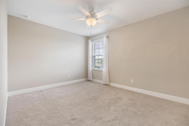 spare room with light colored carpet, baseboards, and ceiling fan