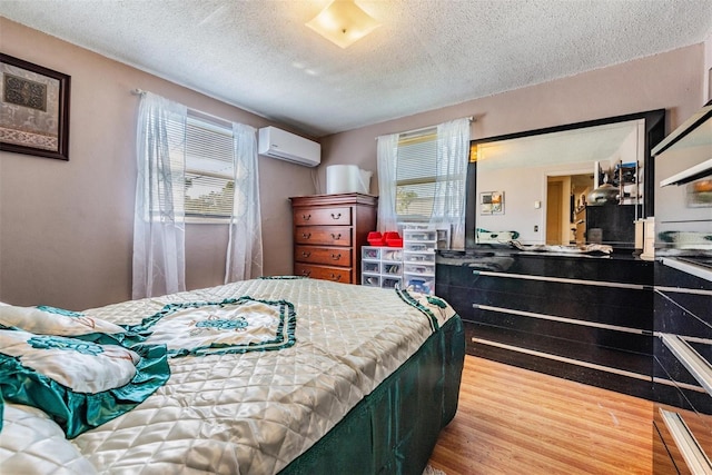 bedroom with a textured ceiling, a wall unit AC, wood finished floors, and multiple windows