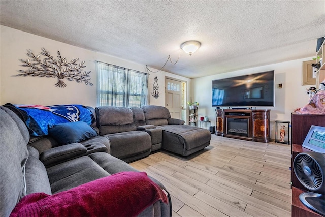 living area featuring a glass covered fireplace, light wood-style flooring, and a textured ceiling