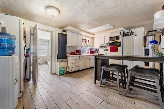 kitchen with a textured ceiling, wall oven, light countertops, a sink, and light wood finished floors