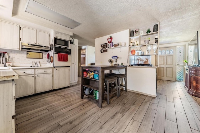 kitchen with open shelves, light wood-style flooring, stainless steel microwave, under cabinet range hood, and white oven