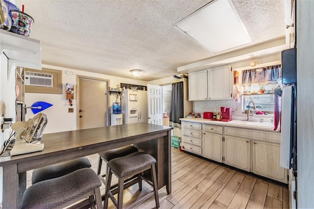 kitchen with a textured ceiling, a wall mounted AC, a sink, light wood-style floors, and white fridge with ice dispenser