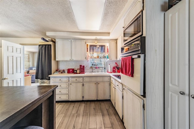 kitchen featuring a sink, light wood-style floors, light countertops, a textured ceiling, and decorative backsplash