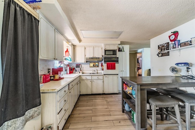 kitchen featuring oven, open shelves, a sink, built in microwave, and light wood-type flooring
