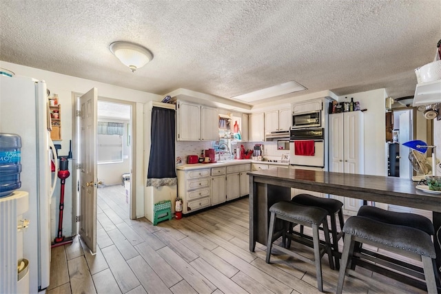 kitchen featuring oven, light countertops, a textured ceiling, freestanding refrigerator, and stainless steel microwave