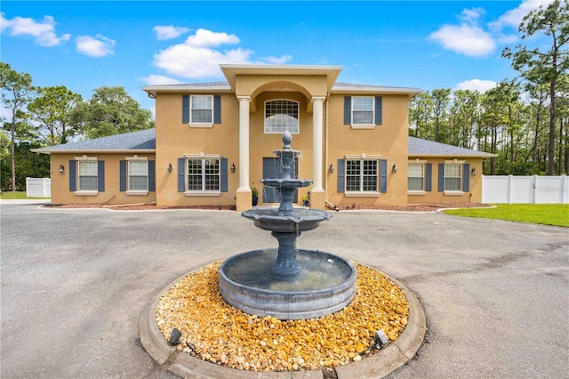 view of front of home with fence, stucco siding, and curved driveway