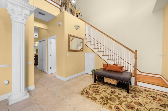 foyer entrance with decorative columns, a high ceiling, stairs, light tile patterned flooring, and baseboards