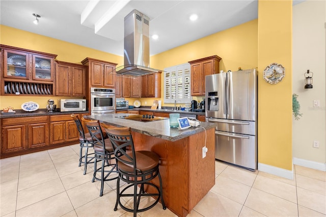 kitchen featuring appliances with stainless steel finishes, island exhaust hood, brown cabinetry, a kitchen bar, and a center island