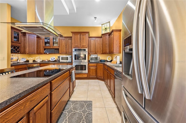 kitchen featuring stainless steel appliances, dark countertops, brown cabinets, island range hood, and glass insert cabinets