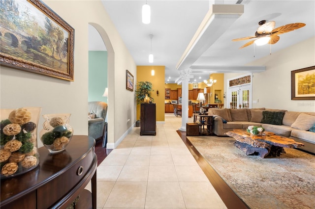 living room with light tile patterned flooring, arched walkways, ceiling fan, ornate columns, and baseboards