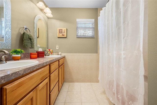 full bathroom featuring tile walls, tile patterned floors, double vanity, and a wainscoted wall