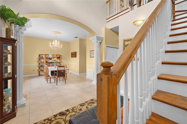 staircase featuring arched walkways, decorative columns, tile patterned floors, baseboards, and a chandelier