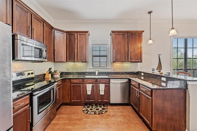 kitchen featuring appliances with stainless steel finishes, a sink, a peninsula, light wood-type flooring, and dark stone countertops
