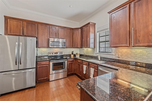 kitchen featuring stainless steel appliances, dark stone counters, light wood finished floors, a sink, and ornamental molding