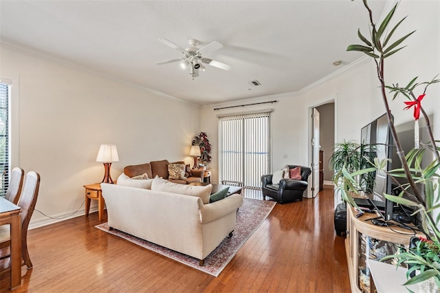 living room featuring a ceiling fan, hardwood / wood-style flooring, crown molding, and baseboards