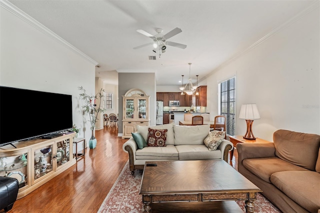 living room featuring crown molding, a ceiling fan, light wood-style flooring, baseboards, and a chandelier