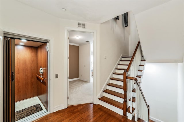 stairs featuring wood finished floors, elevator, and baseboards
