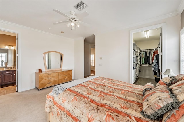 bedroom featuring light colored carpet, ornamental molding, multiple windows, a walk in closet, and ensuite bath