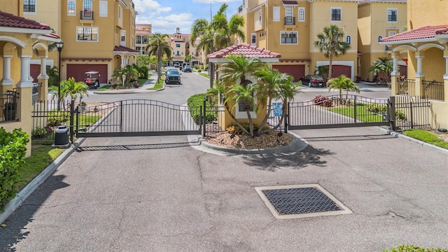 view of asphalt road with a gate, curbs, a residential view, and a gated entry