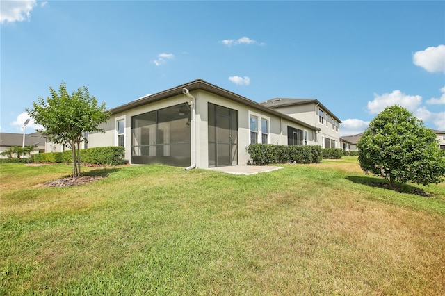 back of house with a lawn, a sunroom, and stucco siding