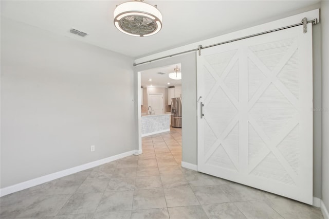 spare room featuring light tile patterned floors, baseboards, a barn door, and visible vents