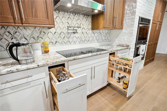 36601 Roberts Rd, Dade City, FL 33525 - kitchen featuring wall chimney range hood, stainless steel double oven, tasteful backsplash, light stone countertops, and black electric cooktop