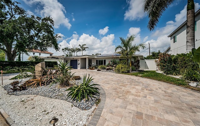 view of front of home with decorative driveway, fence, solar panels, and a gate