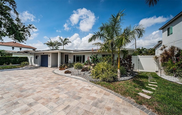 single story home with a garage, decorative driveway, stucco siding, a gate, and roof mounted solar panels