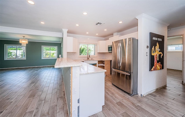 kitchen with crown molding, light wood-style floors, stainless steel appliances, a peninsula, and visible vents