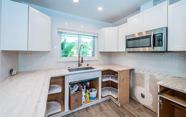 kitchen featuring crown molding, stainless steel microwave, white cabinets, light stone counters, and a sink
