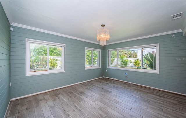 spare room with crown molding, a notable chandelier, plenty of natural light, and wood finished floors
