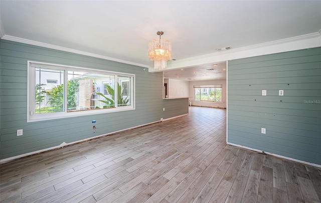spare room featuring visible vents, crown molding, wood finished floors, wooden walls, and an inviting chandelier
