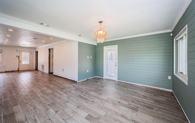 unfurnished living room featuring an inviting chandelier, crown molding, wood finished floors, and visible vents