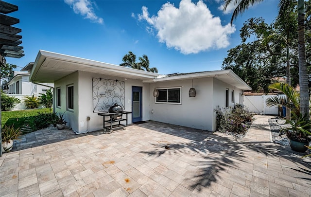 rear view of property featuring a patio, fence, a gate, and stucco siding