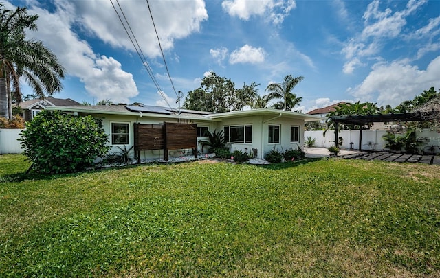rear view of house with a lawn, a fenced backyard, a pergola, and solar panels